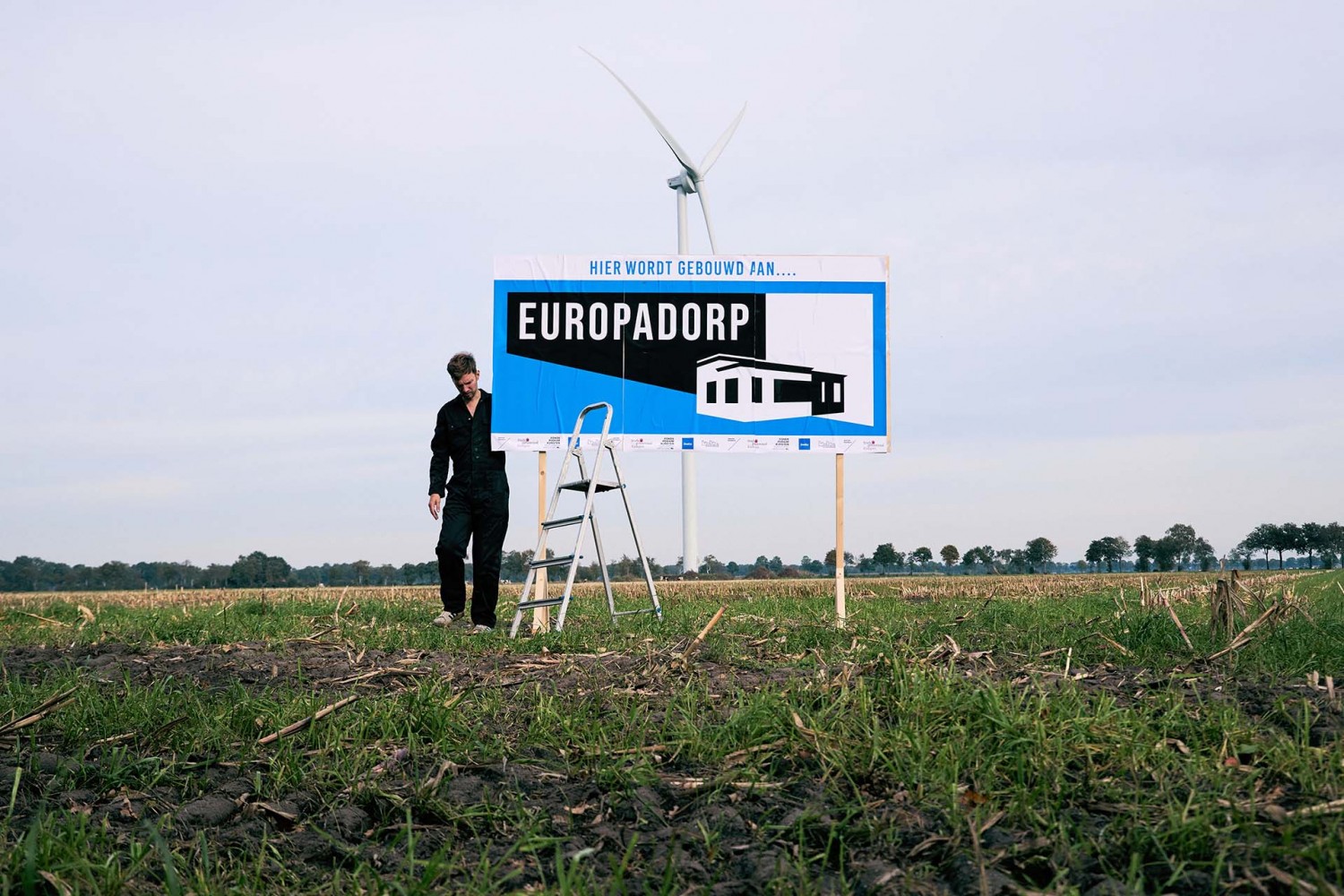 ‘Bouwbord’ van de voorstelling in het Groningse landschap waar het dorp had moeten verrijzen. © Wieger Steenhuis