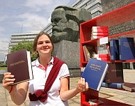 Een studente met een exemplaar van 'Das Kapital', voor een beeld van Marx in Chemnitz, dat in de DDR-tijd Karl-Marx-Stadt heette. Afb: DPA/Picture Alliance